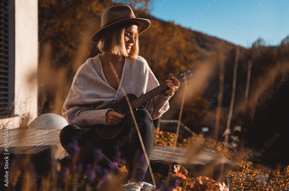 Girl in cowboy hat playing ukulele sitting in home garden patio