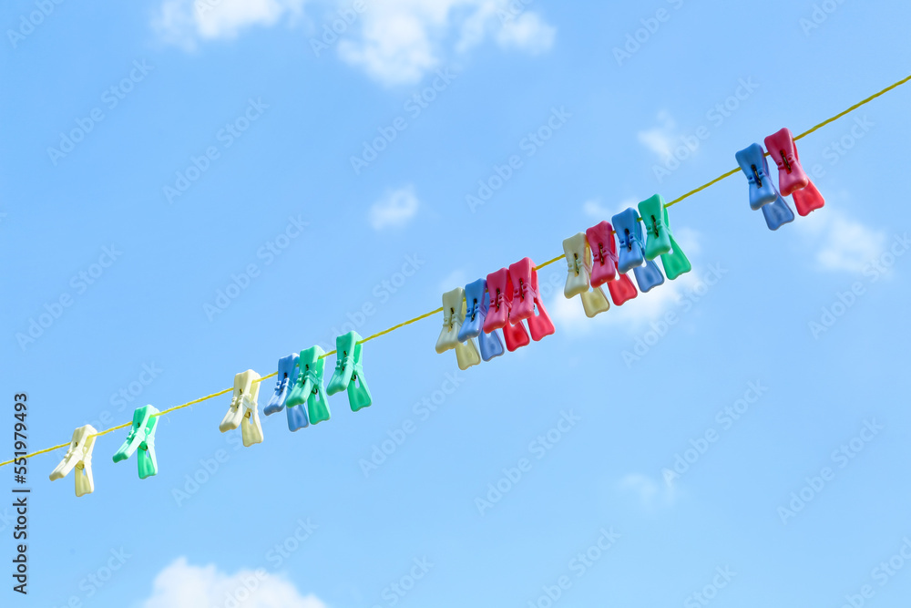 Many different clothespins hanging on rope against blue sky