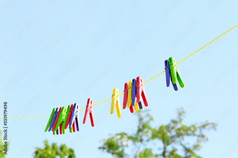 Many plastic clothespins hanging on rope against blue sky