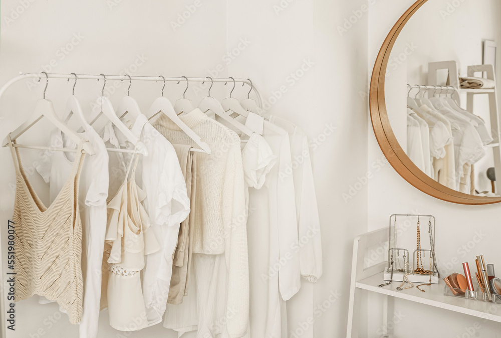 Rack with clothes near light wall in dressing room