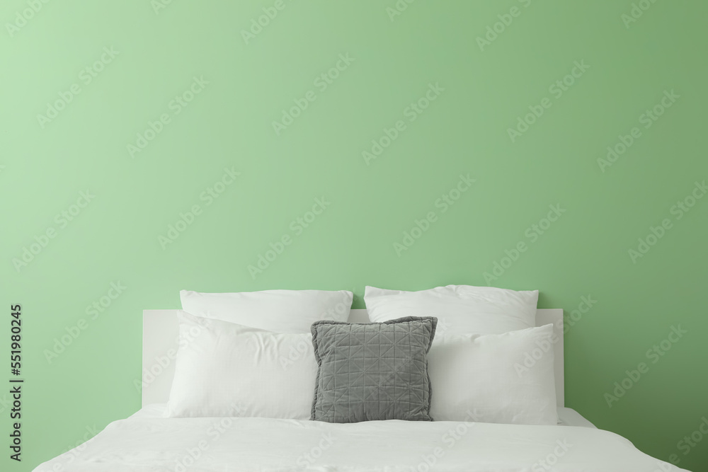 Comfortable bed with soft pillows near green wall