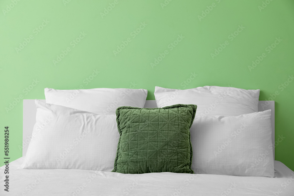 Comfortable bed with soft pillows near green wall