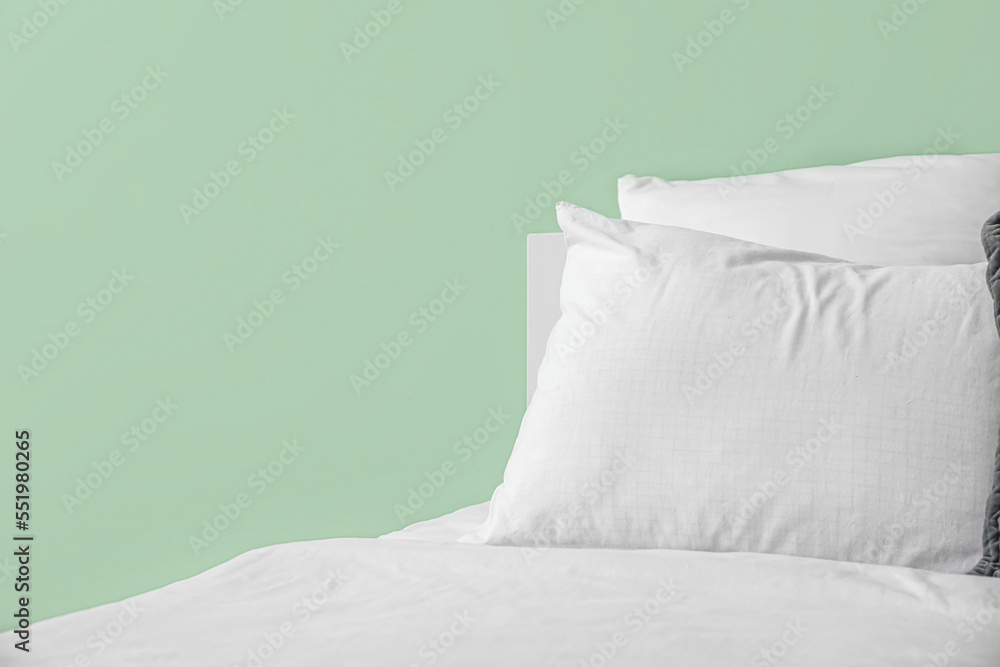 Comfortable bed with soft pillow near green wall