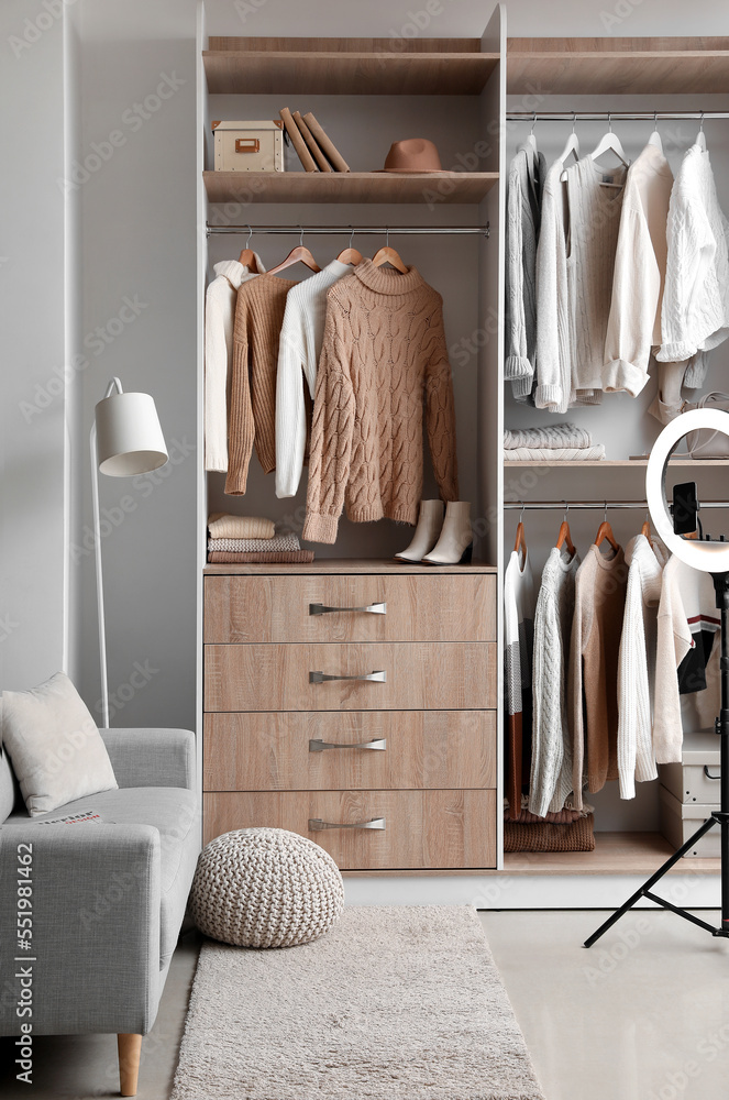 Sofa, ring lamp and sweaters hanging in wardrobe