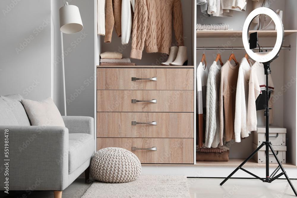 Sofa, ring lamp and sweaters hanging in wardrobe