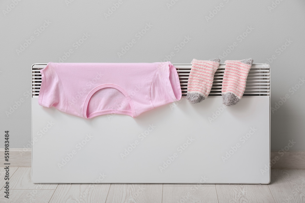 Warm socks and t-shirt drying on electric radiator near light wall