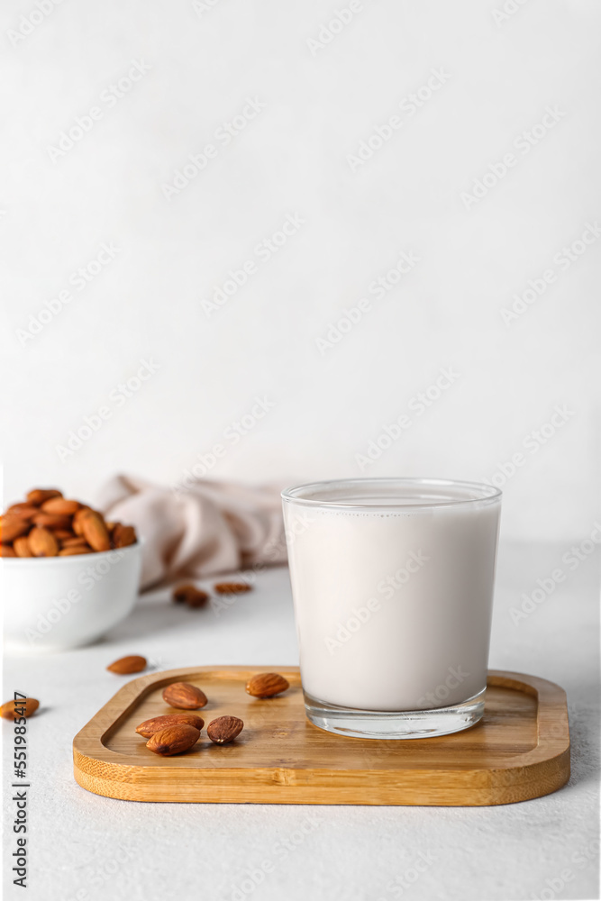 Board with glass of almond milk and nuts on white table