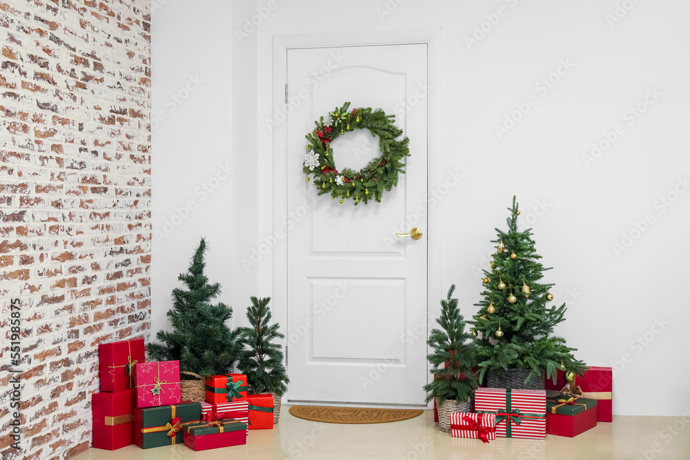 White door with Christmas wreath, fir trees and presents in hall