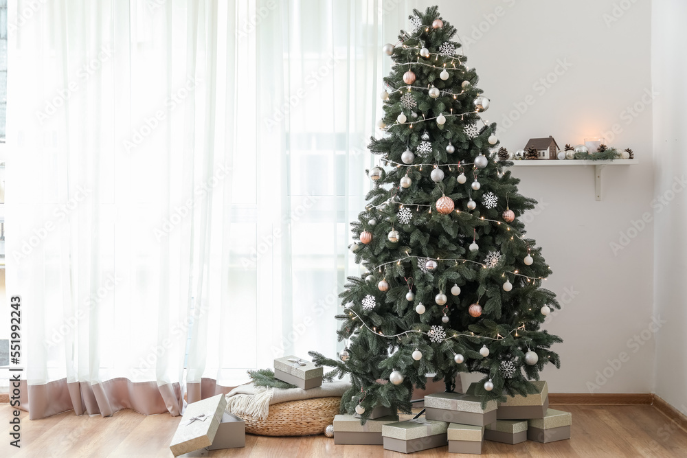 Decorated Christmas tree with pouf and presents near light curtain in living room