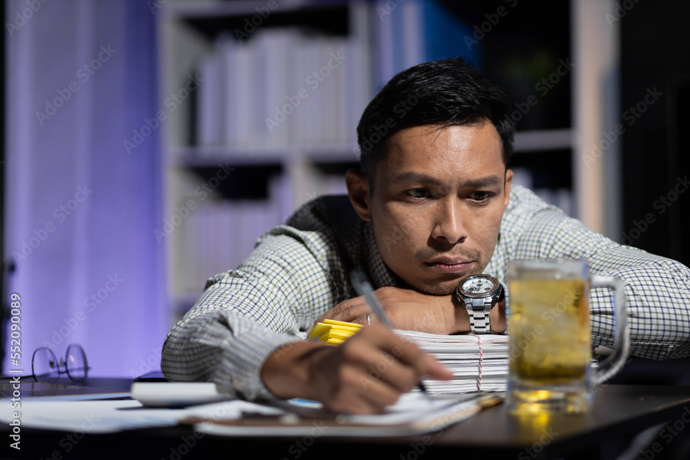 Businessman in the night office drinking beer while working overtime.