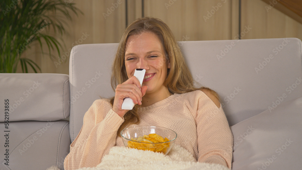 CLOSE UP: Lady smiling while watching entertainment TV program on a comfy sofa