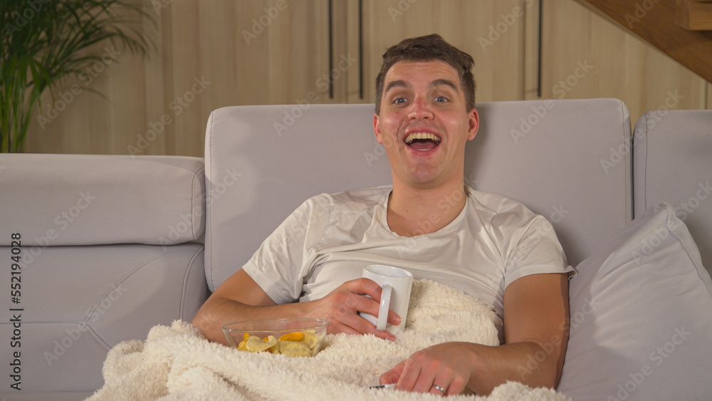 CLOSE UP: Man enjoying on a comfy couch and laughing while watching comedy movie