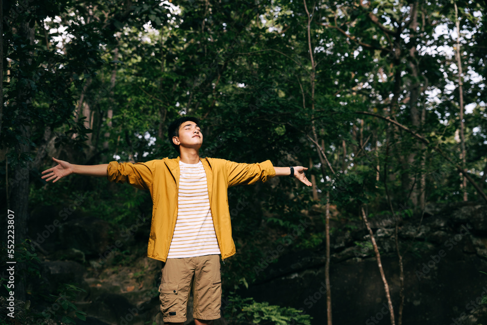 Teenager stands with raised arms in forest. Admiring nature, relaxing.