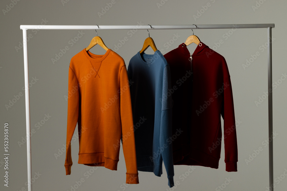 Coloured sweatshirts displayed on clothing rail and copy space on white background