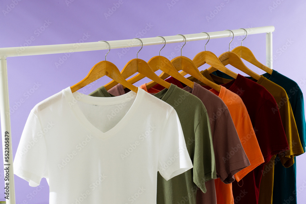 Coloured tshirts displayed on clothing rail and copy space on purple background