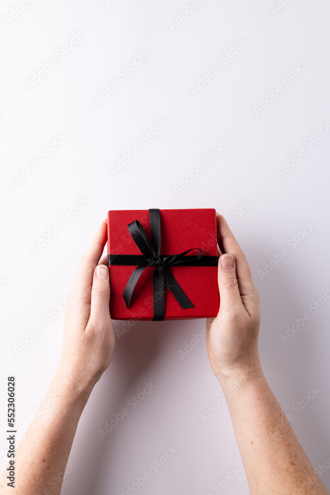 Vertical of hands holding red gift box tied with black ribbon, on white background with copy space