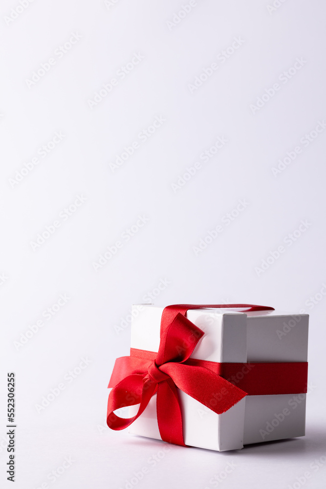 Vertical of white gift box tied with red ribbon, on white background with copy space