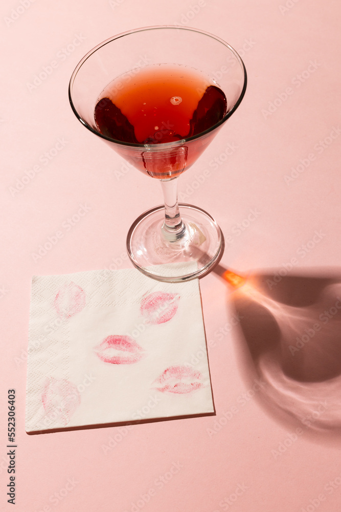 Vertical of red cocktail, with lipstick prints on napkin, on pale pink background with copy space