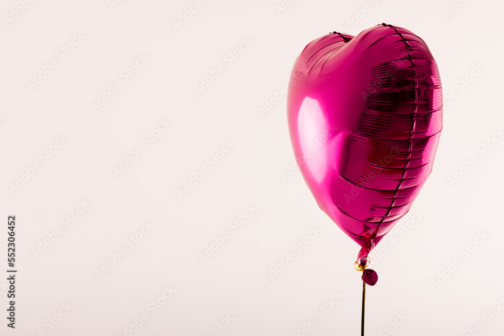 Shiny pink heart shaped balloon floating on white background with copy space