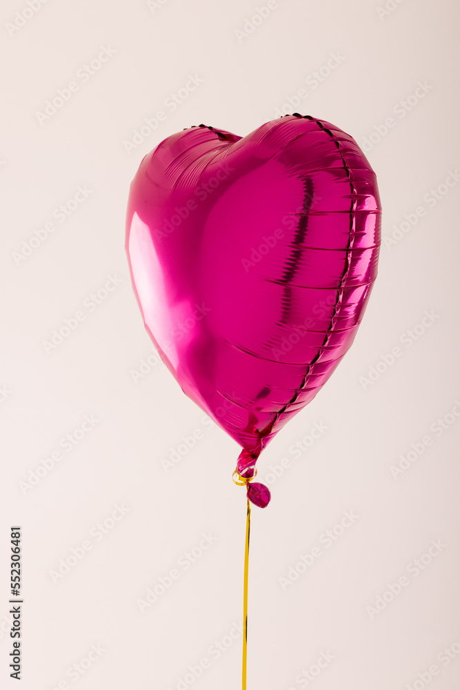 Vertical of shiny pink heart shaped balloon floating on white background with copy space