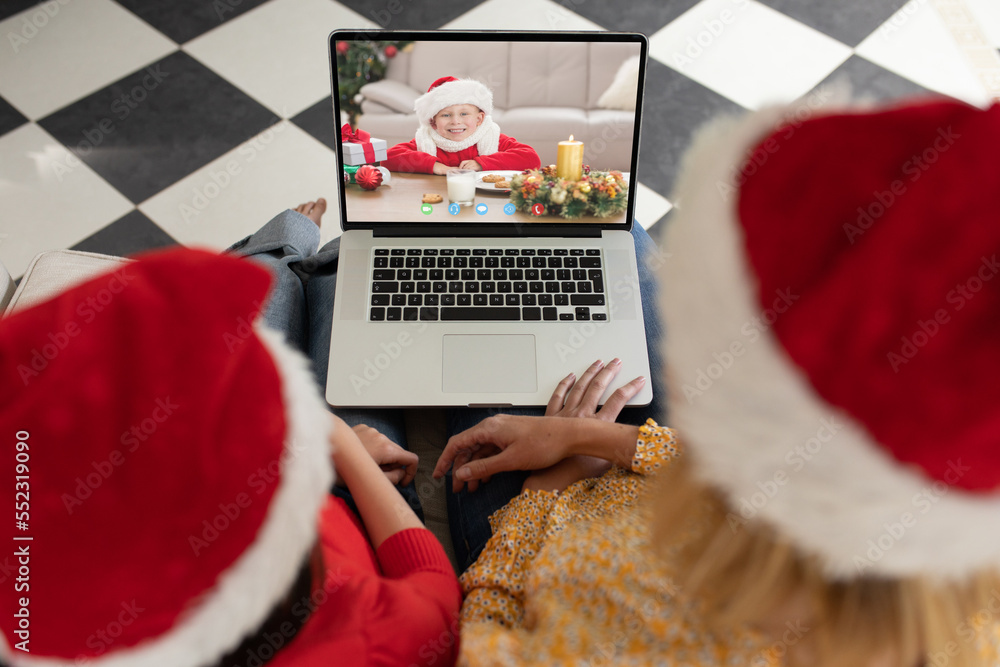 Caucasian mother and daughter in santa hats having christmas laptop video call with caucasian boy