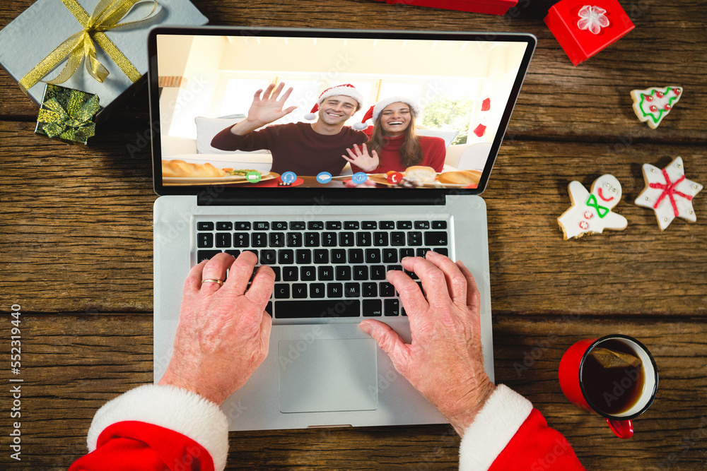 Santa claus with christmas presents having video call with happy caucasian couple