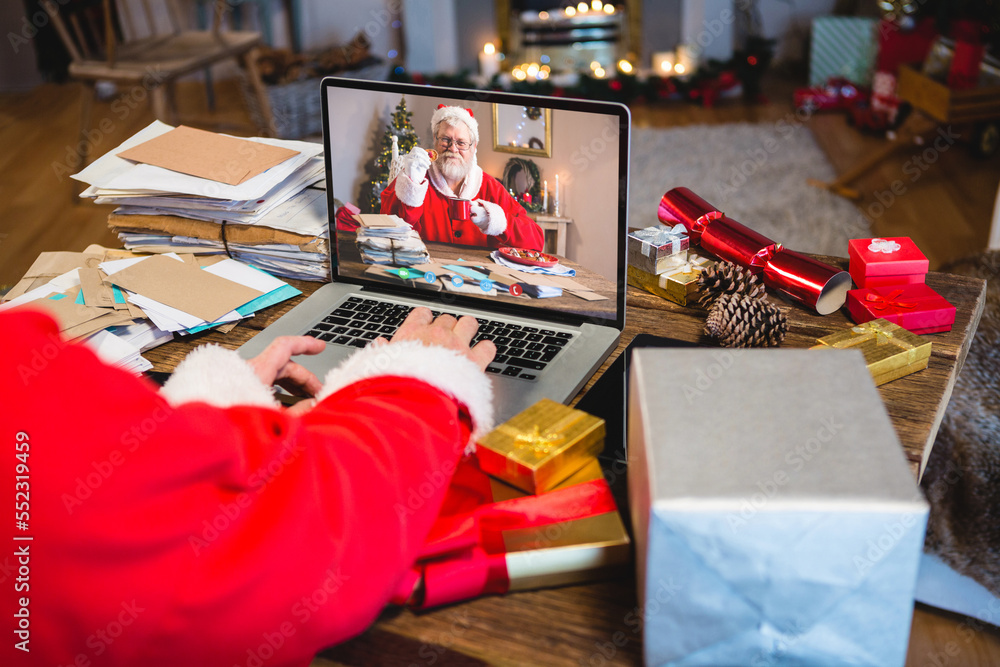 Santa claus with christmas presents having video call with happy caucasian santa claus