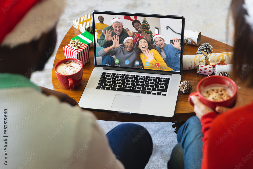 Diverse couple with santa hats having video call with happy diverse friends