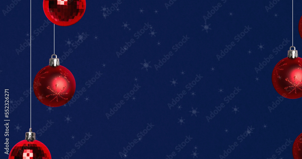 Image of snow falling over christmas bauble decorations on navy background