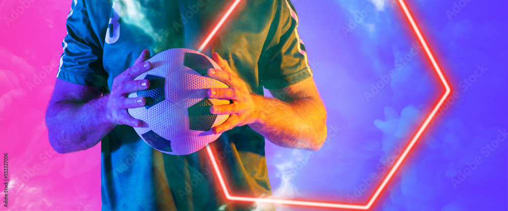 Midsection of biracial male player holding ball with illuminated hexagon shape on colored background