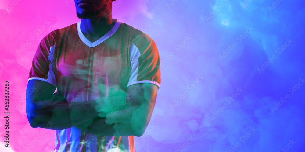 African american male soccer player with arms crossed standing against smoky background