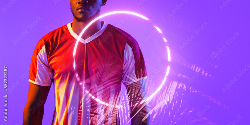 Midsection of african american male soccer player standing by illuminated plant and circle