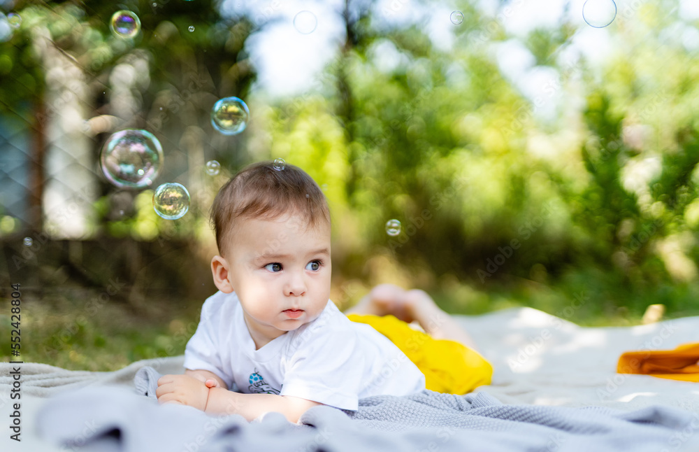 Little baby playing on a blanket in the park on a sunny day. Real life shot of a baby. Outdoor fun f