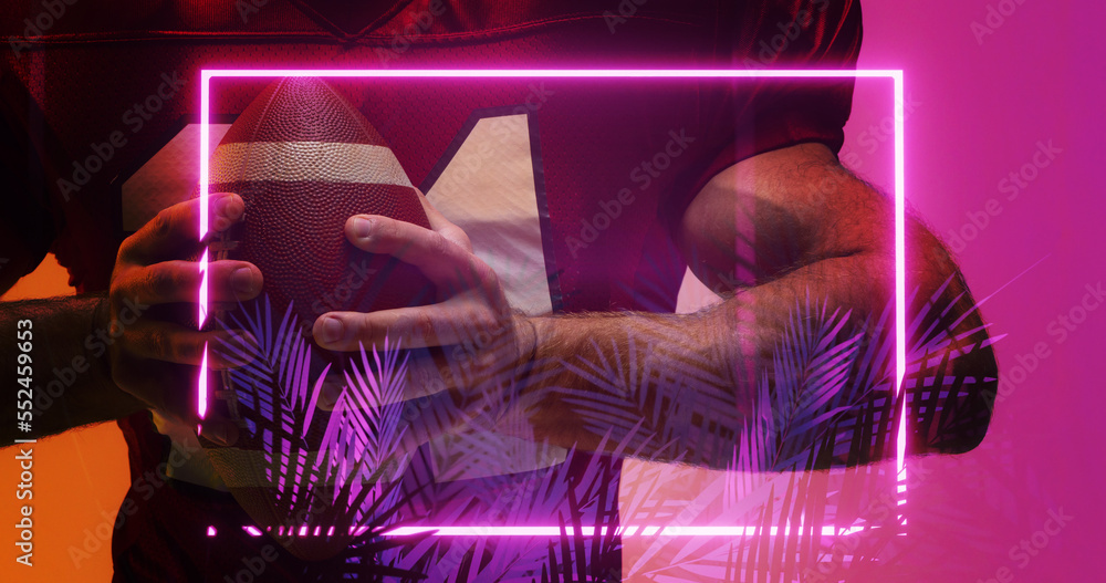 Midsection of american football player holding ball standing by illuminated rectangle and plants