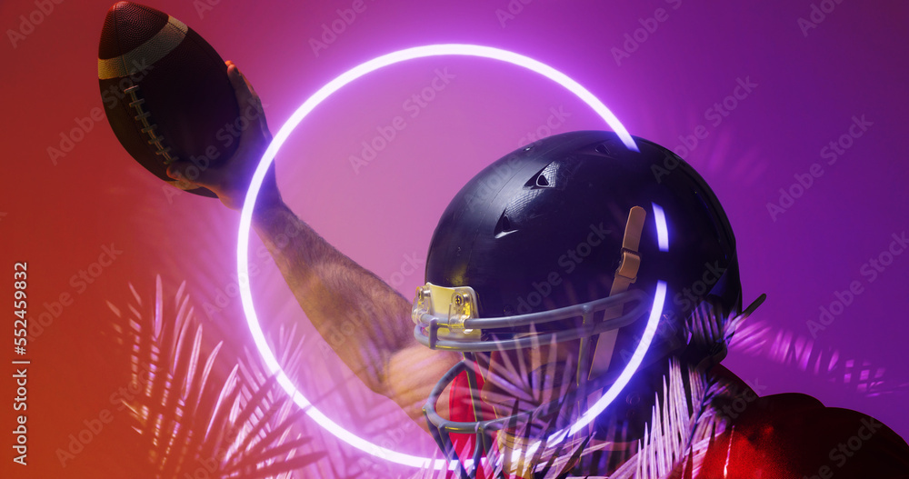 Close-up of american football player wearing helmet raising hand with ball by circle and plants