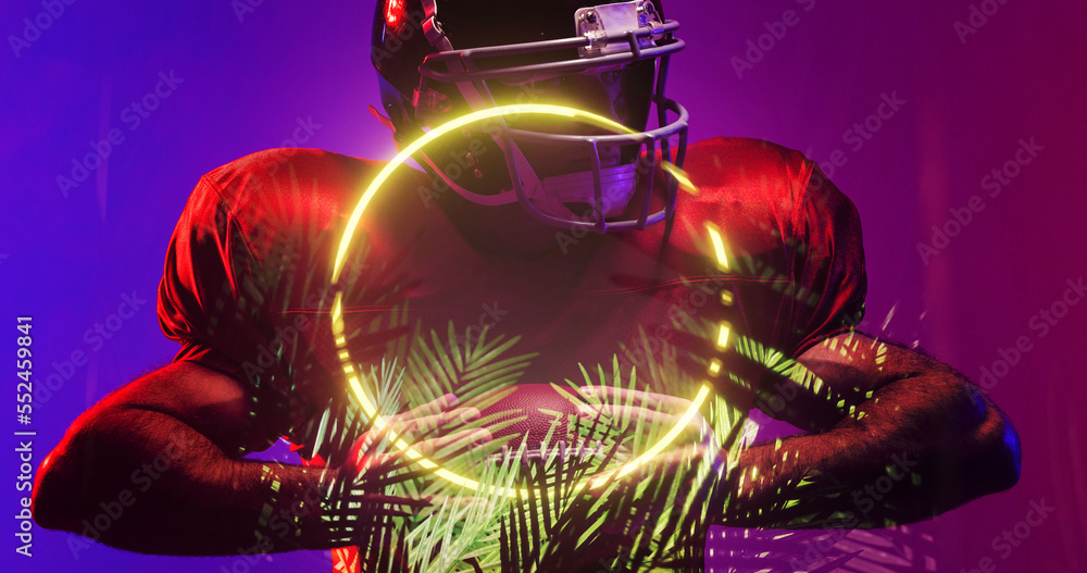 American football player wearing helmet and holding ball by illuminated circle and plants