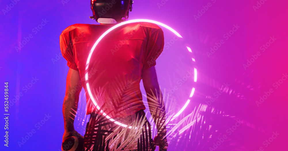 Rear view of american football player wearing red uniform standing by illuminated circle and plants