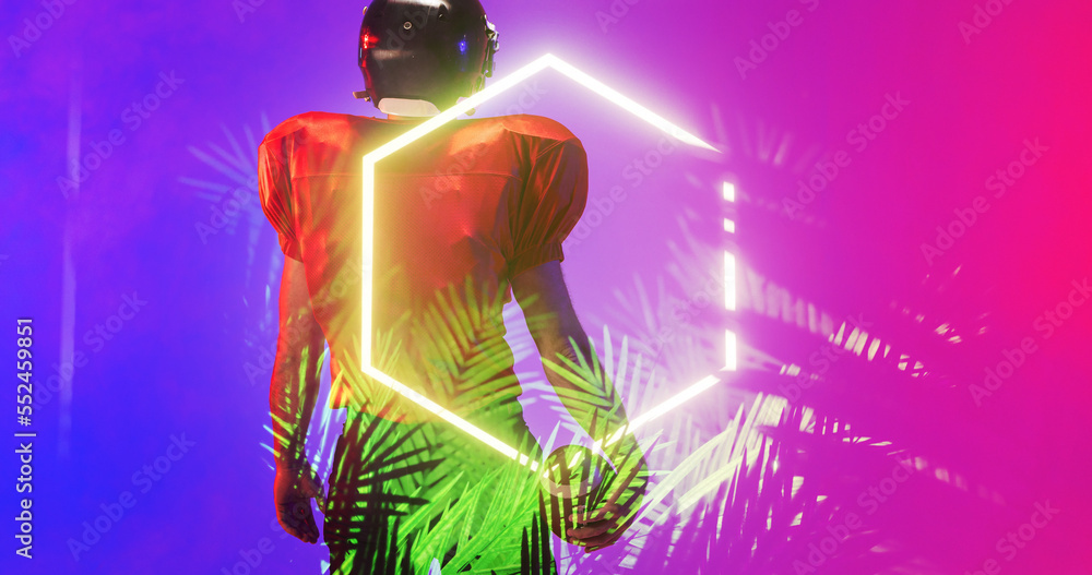 Rear view of american football player in uniform standing amidst plants and illuminated hexagon