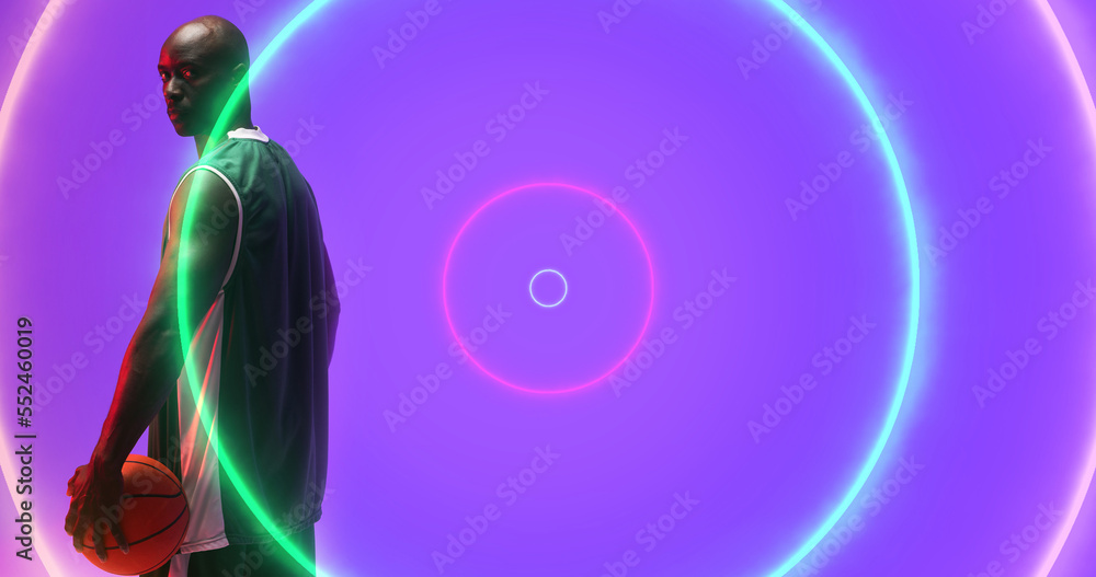 Bald african american basketball player with ball standing by illuminated colorful circles