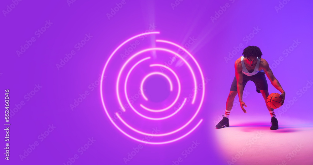 Composite of biracial male player playing basketball by illuminated circular pattern, copy space