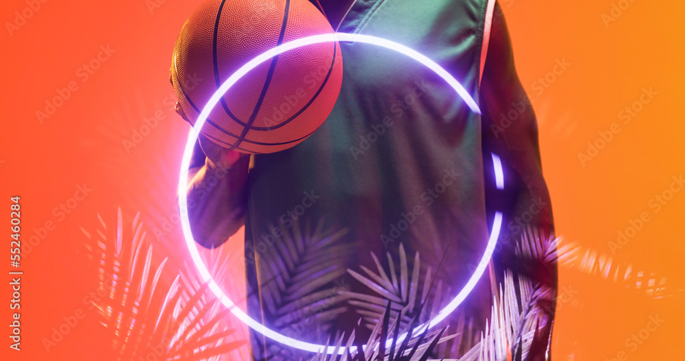 Midsection of african american basketball player with ball by illuminated circle and plants