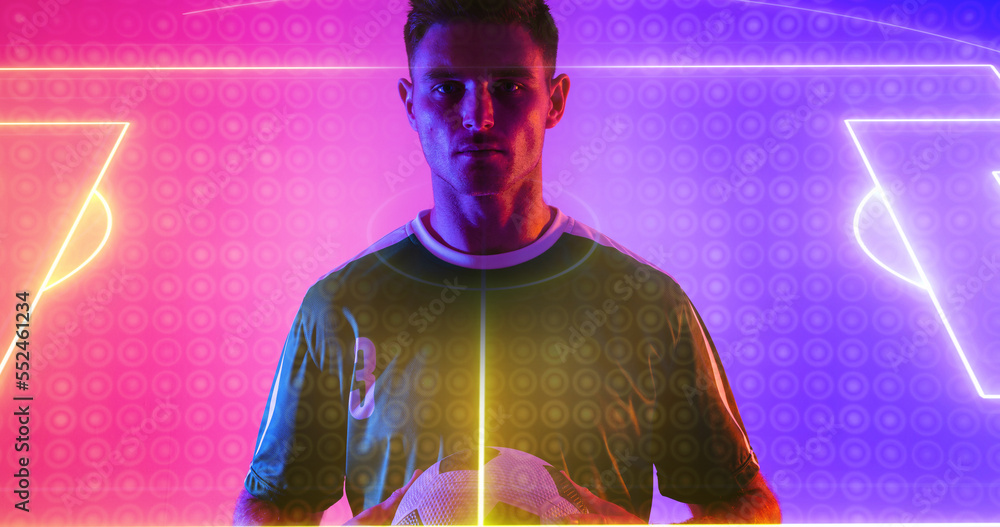 Portrait of caucasian player holding ball with neon soccer field in blue and pink background