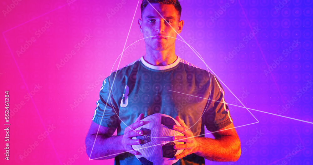 Portrait of determined caucasian athlete holding soccer ball with geometric neon design, copy space