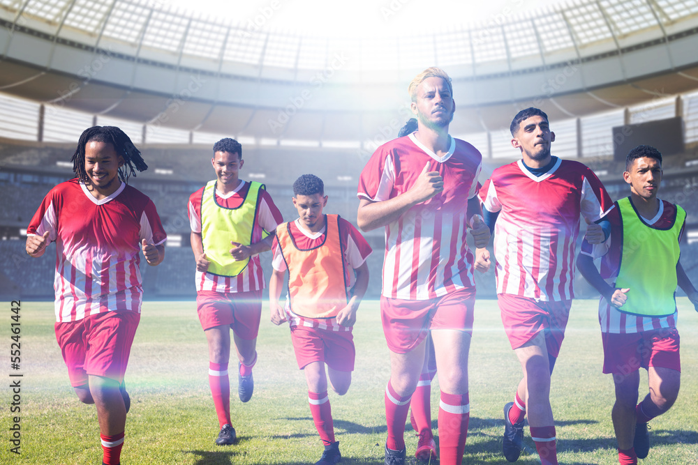 Team of multiracial male soccer players in sports clothing running in stadium