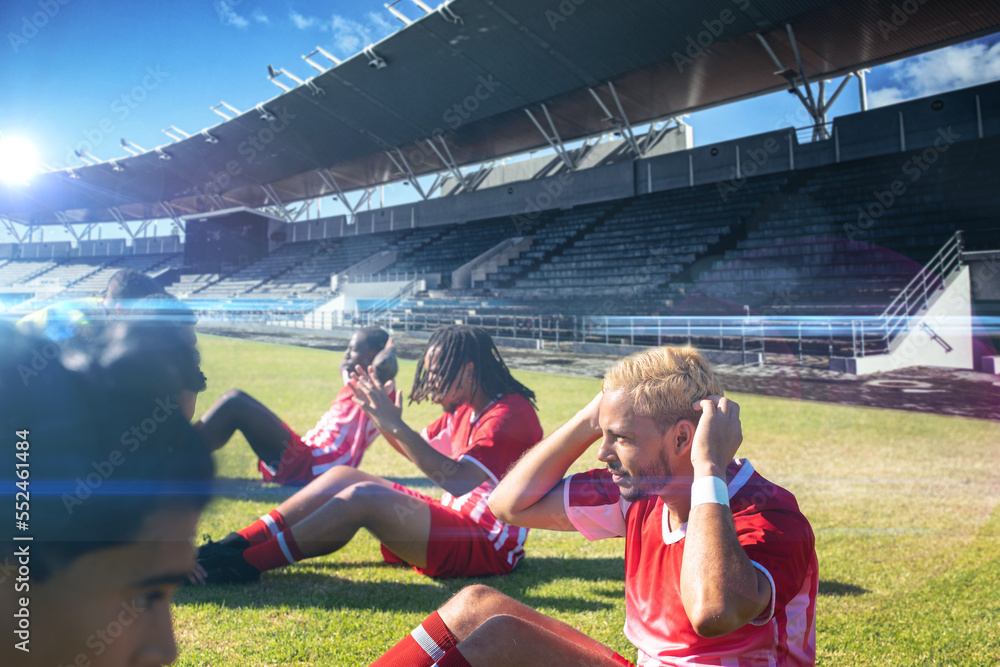 Team of multiracial male soccer players in exercising in stadium on sunny day