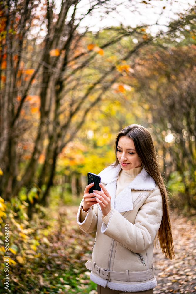 Pretty lady with phone in the park. Beautiful young woman using phone in nature.