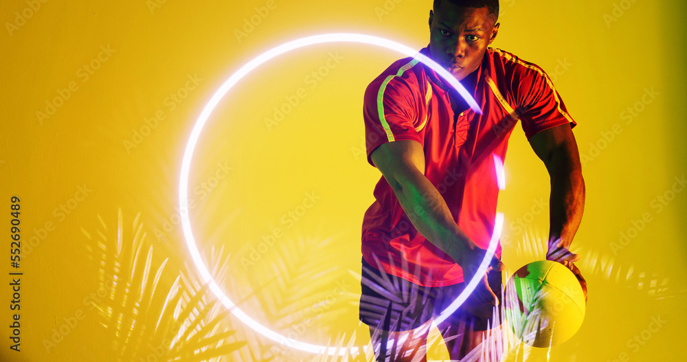 Illuminated circle with plants and african american rugby player holding ball on yellow background