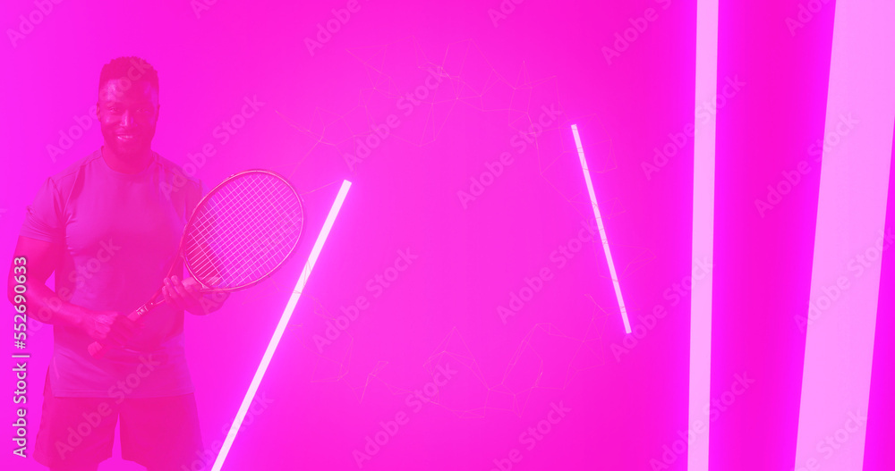 African american male player holding racket and standing by illuminated lines on pink background