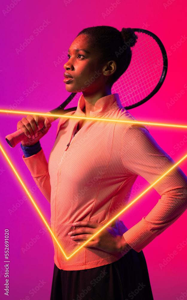 African american female tennis player with hand on hip holding racket by illuminated triangle