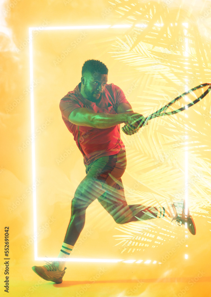 African american male player playing tennis with racket by illuminated rectangle and plants